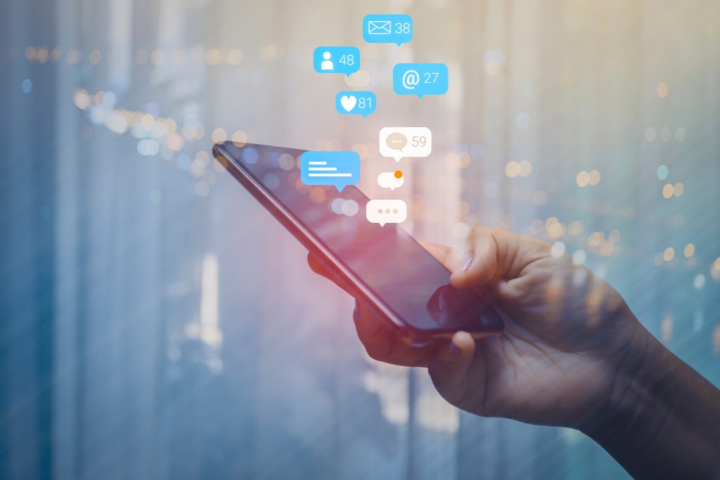 Hand holding an iPhone managing social media platforms.